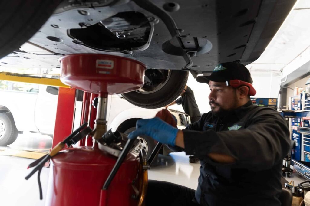 A technician performing an oil change under a vehicle on the lift at Chuck's Auto Repair