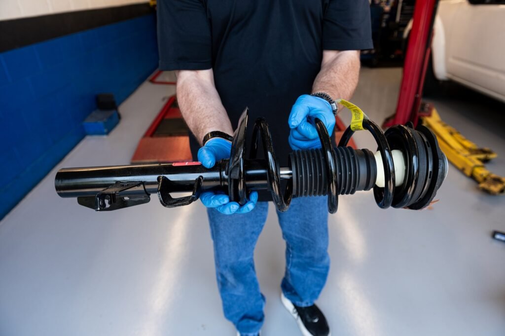 Technician holding a new complete strut assembly (pre-assembled with new spring and mount) before installation during strut replacement at Chuck's Auto Repair in North Seattle