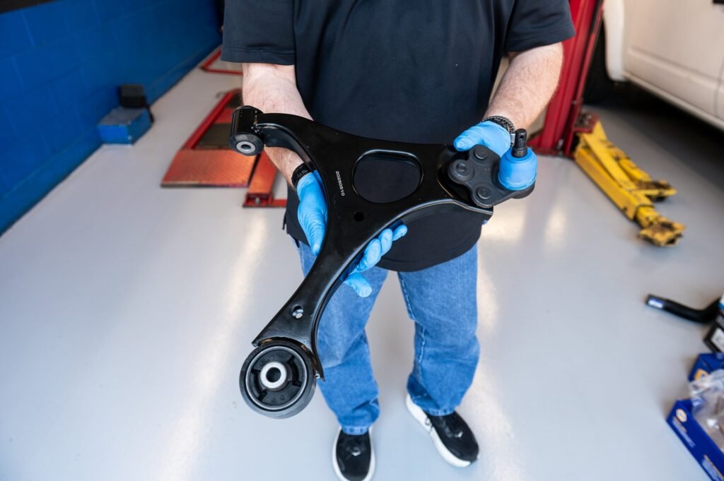 Technician holding a new lower control arm with ball joint (new bushings and sealed ball joint) before installation during control arm replacement at Chuck's Auto Repair in North Seattle