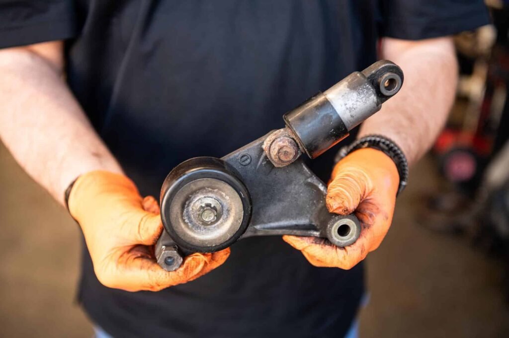 Technician holding a serpentine belt tensioner assembly — seized pulley/weak damper during serpentine belt service at Chuck's Auto Repair in North Seattle