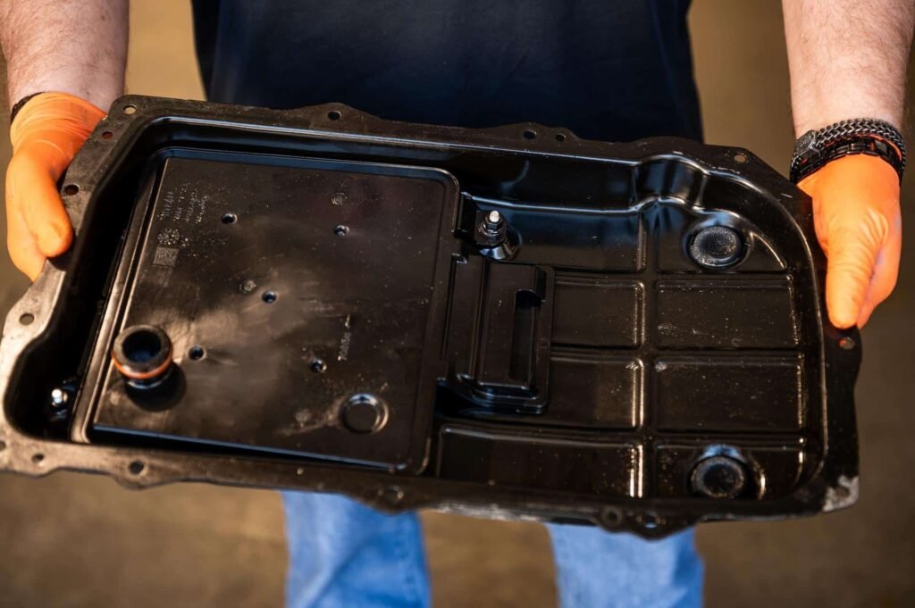 Technician holding an automatic transmission oil pan with internal filter — replaced during service during transmission fluid service at Chuck's Auto Repair in North Seattle