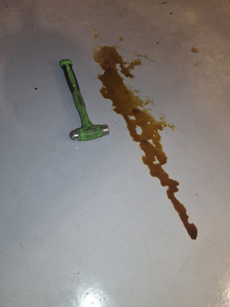Oil trail on a shop floor next to a green-handled hammer during a Ford F-150 inspection.