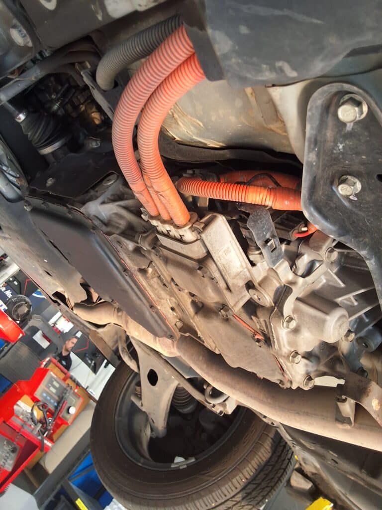 CVT transmission and orange hybrid-system cabling underneath a 2014 Subaru XV Crosstrek Hybrid.