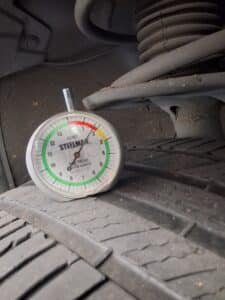 Tread-depth gauge showing approximately 1.5/32 inch on the front-right tire of a 2013 Toyota RAV4.