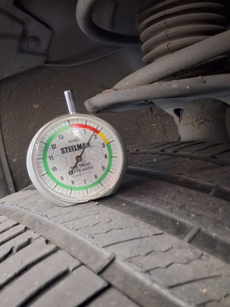 Tread-depth gauge showing approximately 1.5/32 inch on the front-right tire of a 2013 Toyota RAV4.