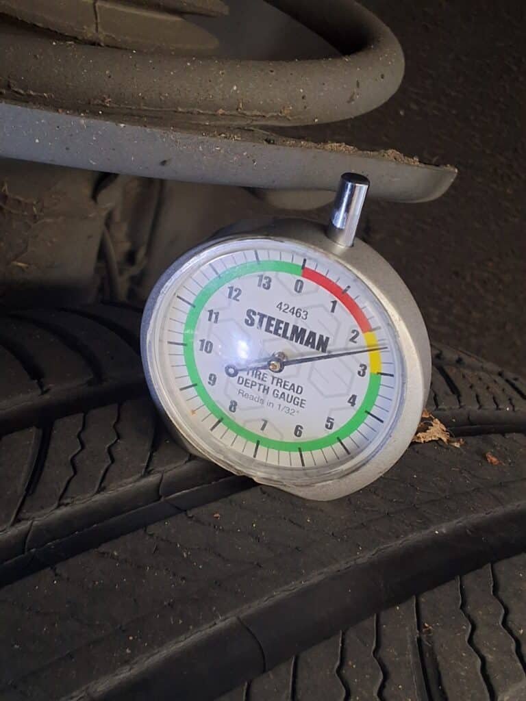 Tread-depth gauge showing approximately 2.5/32 inch on the front-left tire of a 2013 Toyota RAV4.