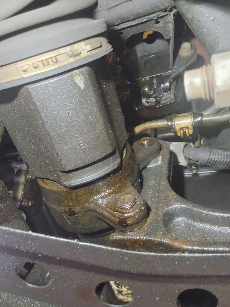 Heavy oil residue visible on the engine of a high mileage Toyota Tacoma during inspection.